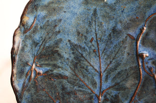 a close up of a blue vase with leaves on it