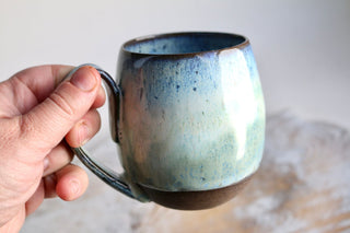 a hand holding a blue and green coffee mug