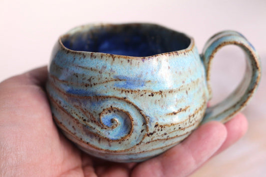 a hand holding a blue ceramic cup with a swirl design