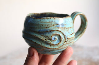 a hand holding a blue ceramic cup in it's palm