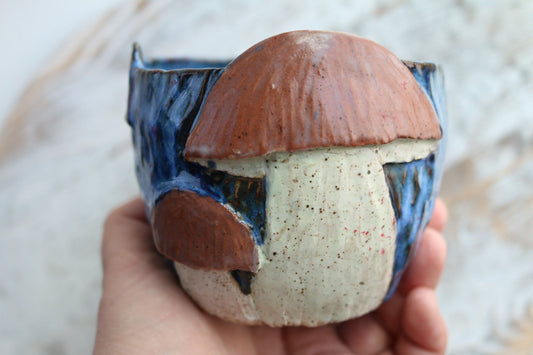 a hand holding a ceramic cup with a mushroom on it