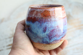 a hand holding a cup with a blue and red design on it