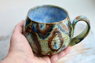 a hand holding a coffee cup with a brown and blue design on it
