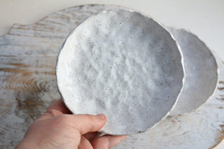 a person holding a white bowl on top of a wooden table