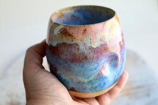 a hand holding a cup with a blue and pink design on it