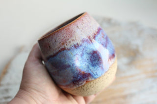 a hand holding a cup with a blue and red design on it