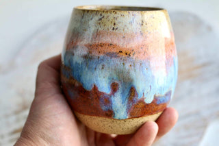 a hand holding a ceramic cup with a blue and orange design