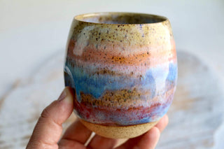 a hand holding a ceramic cup with a multicolored design