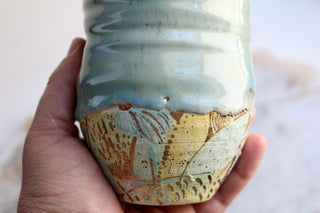 a hand holding a ceramic vase with a painting on it