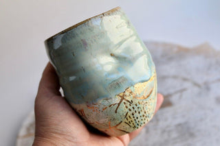 a hand holding a ceramic cup with designs on it