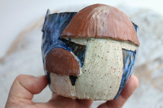 a hand holding a ceramic figurine of a mushroom