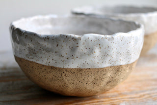 two white and brown bowls sitting on top of a wooden table