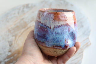 a hand holding a small cup with a blue and red design on it