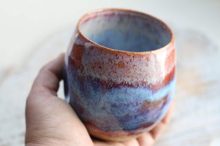 a hand holding a cup with a blue and red design on it