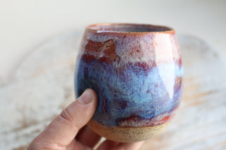 a hand holding a cup with a blue and red design on it