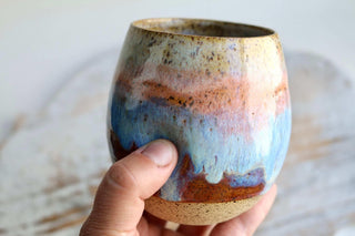 a hand holding a ceramic cup with a blue and brown glaze