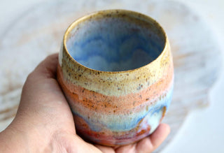 a hand holding a ceramic cup on a table