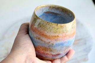 a hand holding a ceramic cup on top of a table