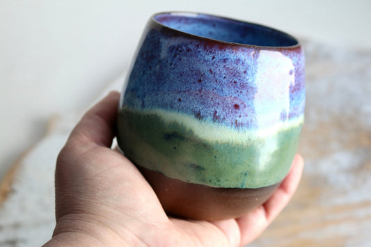 a hand holding a blue and green cup