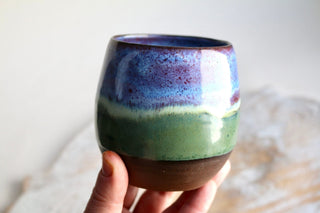 a hand holding a cup with a multicolored design