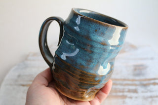 a hand holding a blue and brown coffee cup